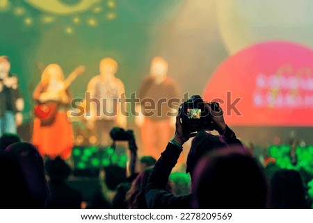 Silhouette of spectator, photographer taking picture with camera at concert, bright colorful light by stage lights