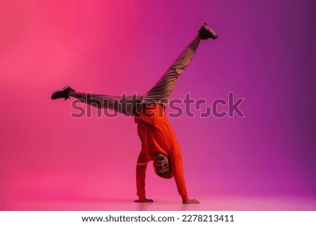 Young african man wearing hoodie doing handstand while dancing isolated over over pink neon studio background