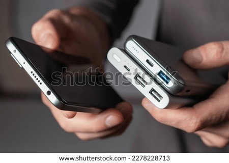the man is holding the phone and the charger. Powerbank and smartphone in hand. Power-saving device power bank smartphone Royalty-Free Stock Photo #2278228713