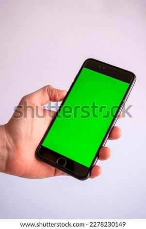 Hand holds a mobile phone with a blank green screen to add various contents