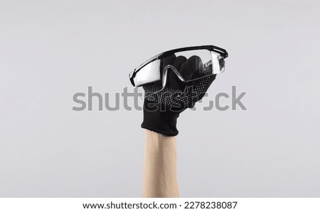 Female hand in working fabric glove holding protective glasses on gray background Royalty-Free Stock Photo #2278238087