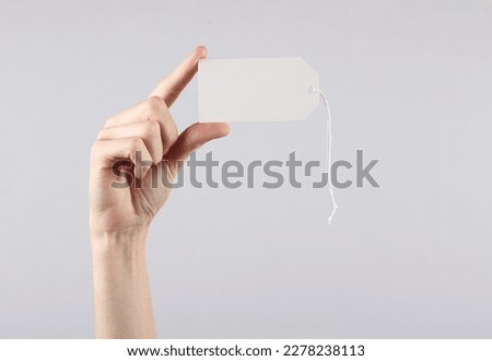 Female hand holds a white blank price tag on gray background. Sale concept