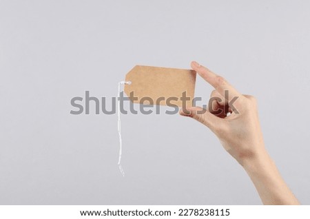 Female hand holds craft blank price tag on gray background. Sale concept