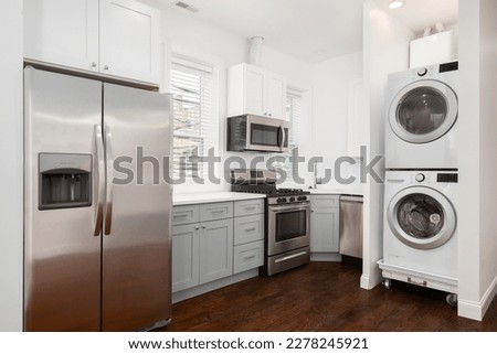 An apartment kitchen with white and grey cabinets, stainless steel appliances, and a stacked washer and dryer. No brands or names. Royalty-Free Stock Photo #2278245921