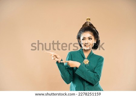 asian woman in green kebaya standing and pointing with her fingers on isolated background