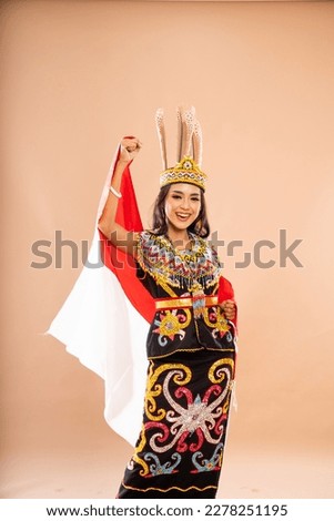 asian woman in traditional clothes of dayak tribe holding the indonesian flag behind her body on isolated background