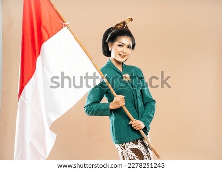 smiling asian woman in green kebaya standing holding the indonesian flag on isolated background