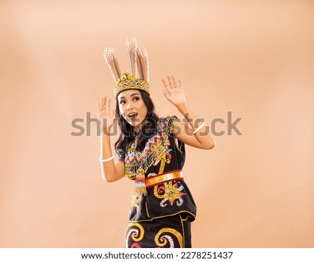 shocked asian woman in traditional outfit of dayak tribe standing and raising her hands on isolated background