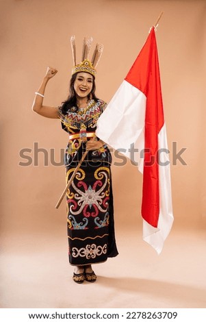 happy asian woman in king bibinge clenched her arm while holding the indonesian flag on isolated background