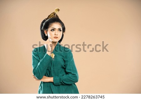 javanese woman in green kebaya standing with solemn face and touch her cheek on isolated backgroun