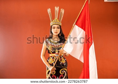 asian woman in king bibinge standing with solemn face and holding the indonesian flag on isolated background