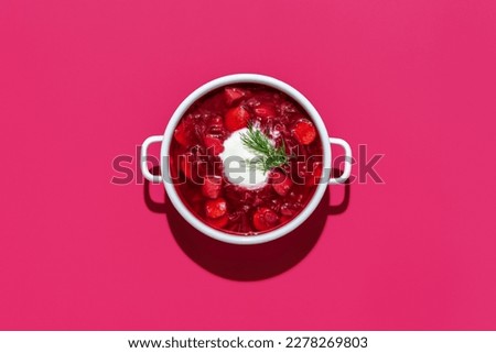 Top view with a bowl of ukrainian borscht with sour cream, isolated on a pink background. Homemade beetroot soup and other vegetables, minimalist on a vibrant colored table. Royalty-Free Stock Photo #2278269803