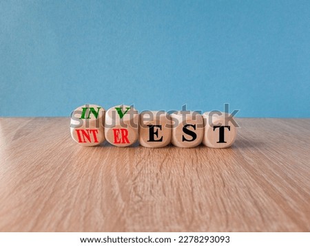 Invest or interest symbol.  Turned wooden cubes and changes the word 'invest' to 'interest'. Beautiful wooden table, bue background, copy space. 