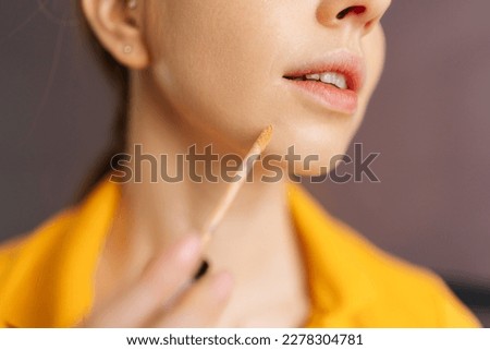 Detail close-up of unrecognizable young woman with natural beauty applying foundation on face to correct skin and hide pimples near lips. Female doing makeup putting base tone cream using concealer. Royalty-Free Stock Photo #2278304781