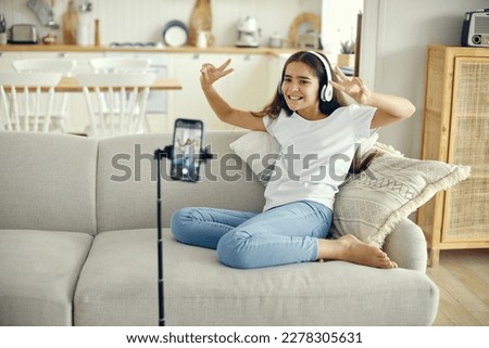 Pretty preteen girl blogger sit on sofa greeting virtual friends, record video for vlog, make call, lead stream with friends use modern tech. Streamer activity, igeneration, fun and home use internet  Royalty-Free Stock Photo #2278305631