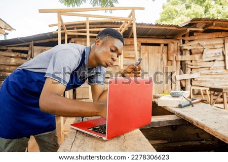 african carpenter holding his credit card wearing an apron paying with his laptop and credit card