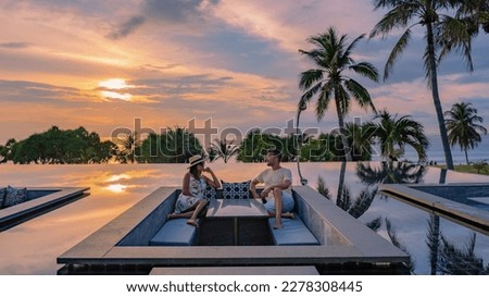 couple watching the sunset in an infinity pool on a luxury vacation in Thailand, man and woman watching the sunset on the edge of a pool in Thailand on vacation Royalty-Free Stock Photo #2278308445