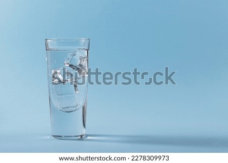 Glass of pure cold sparkling water with ice cubes on light blue background. Free space for text