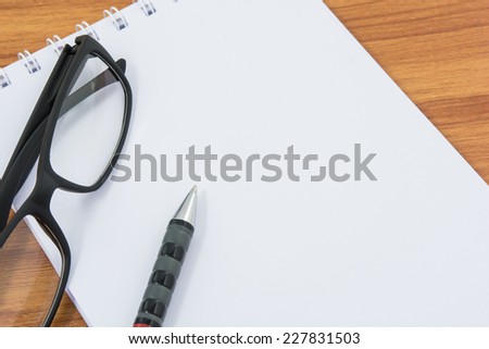Notebook, pen and glasses on wooden table