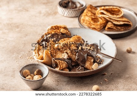 Crepes with chocolate and hazelnuts on beige background. Thin pancakes as delisious breakfast or dessert concept, Pancake day, Maslenitsa. Horisontal Royalty-Free Stock Photo #2278322685