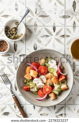 Traditional italian tomato salad panzanella with mozzarella, capers, red onion, croutons, cucumbers and basil served for a person. Summer salad on printed tile background with copy space, top view Royalty-Free Stock Photo #2278323237