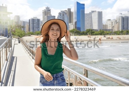 Stylish girl with hat walking along promenade on windy day with skyline skyscrapers on the background, Santos, Brazil