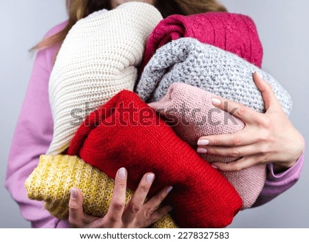 A woman holds bright warm winter sweaters. Closet cleaning. Donations. Close-up. Selective focus.