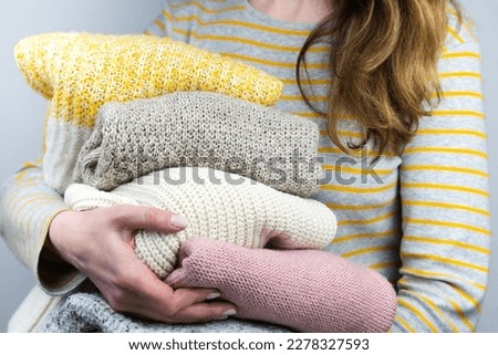 A young woman holds knitted warm sweaters in her hands. Autumn and winter clothes. Decluttering. Donations. Close-up. Selective focus.