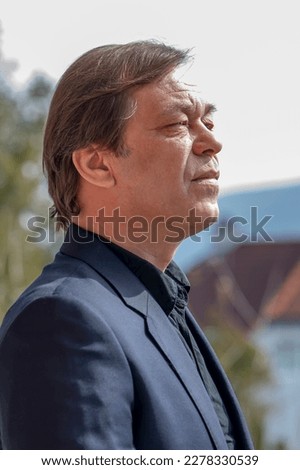 Street portrait of a man 40-50 years old in a black suit on a neutral blurred background, vertical photo, side view. Perhaps he is a buyer, an actor, a military pensioner, the head of a company,  Royalty-Free Stock Photo #2278330539