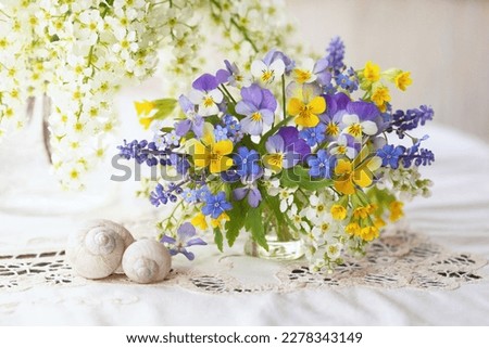 A bouquet of spring blue, yellow, white, violet flowers in a vase on the table. Pansies, forget me nots, primroses, bird cherry, violets, muscari. Postcard, blur, selective focus.