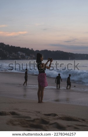 Woman photographs a sunset on the ocean with a camera.