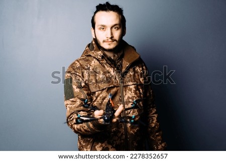 Soldier in military camouflage uniform holding fpv racing kamikaze drone bomber on blue background.