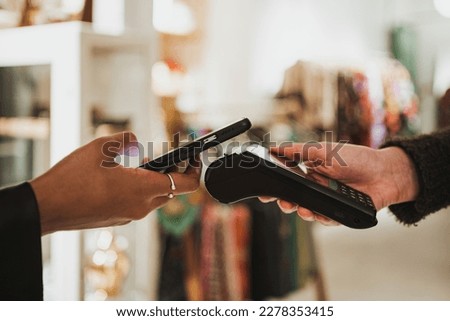 Close up shot of young woman paying contactless on a POS in a shop. She is using her phone. Royalty-Free Stock Photo #2278353415
