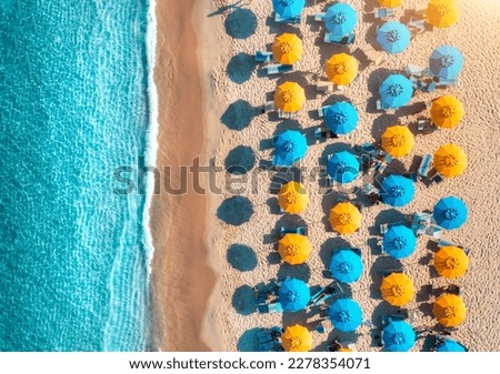 Aerial view of yellow and blue umbrellas on empty sandy beach, blue sea at sunset in summer. Tropical landscape with turquoise water. Travel and vacation in Sardinia, Italy. Top view from drone Royalty-Free Stock Photo #2278354071