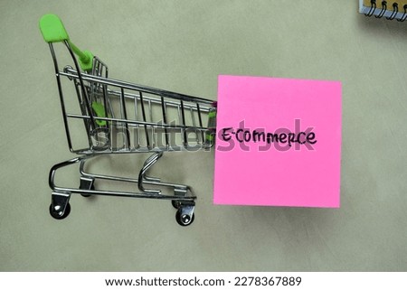Concept of E-Commerce write on sticky notes with trolley isolated on Wooden Table.