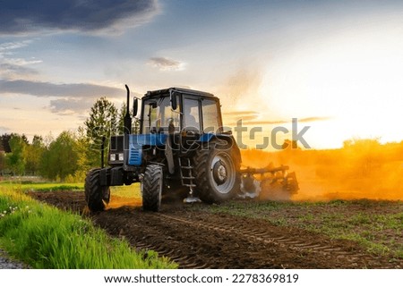 Modern blue tractor machinery plowing agricultural field meadow at farm at spring autumn during sunset. Farmer cultivating,make soil tillage before seeding plants,crops,nature countryside rural scene. Royalty-Free Stock Photo #2278369819