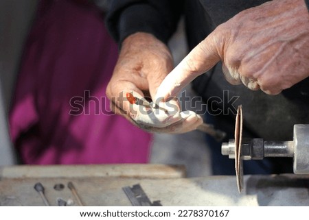 Hands of elderly craftsman man working in a workshop polishing opal stones and minerals to form precious jewelry
