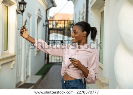 An attractive young black African woman taking phone selfie with excitement while holding bank credit card for online transaction