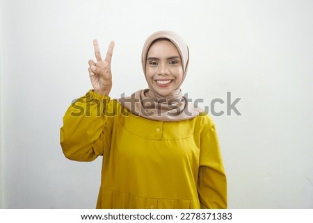 Cheerful young Asian woman in yellow dress showing peace sign ov