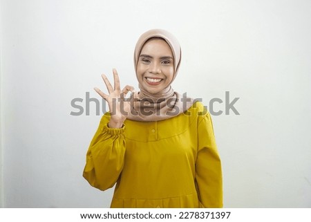 Smiling young Asian woman in white casual showing okay gesture demonstrates symbol of approval isolated over white background