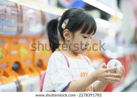 Cute young Asian girl smiling and happy after picking the toy out from Gachapon machine in mall, tourist attraction, vacation activity. kid leisure.