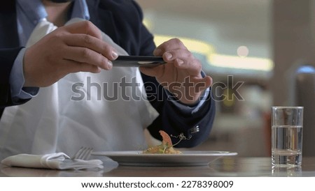 Hungry man rubbing hand before eating and taking white napkin in gourmet restaurant. Man making photo dish with food on mobile phone in trendy cafe