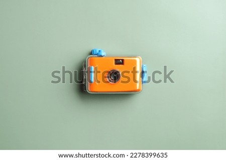 Orange pocket camera or  film camera in waterproof case  on green paper background with copy space. Minimal concept.