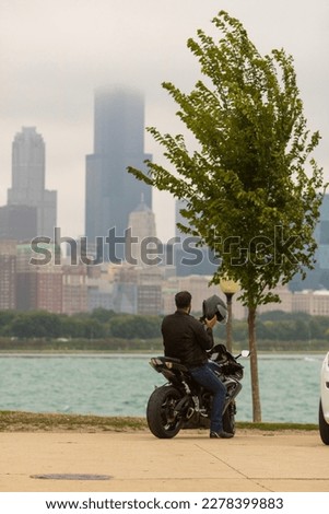A person on a motorcycle holding his helmet next to the lake looking at the Chicago, Illinois skyline.