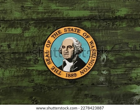 The state seal of Washington, USA, featuring George Washington in the center, is shown mounted on a rustic wood wall painted green.