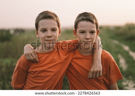 Funny twin brother boys in orange t-shirt playing outdoors on field at sunset. Happy children, lifestyle. Royalty-Free Stock Photo #2278426563
