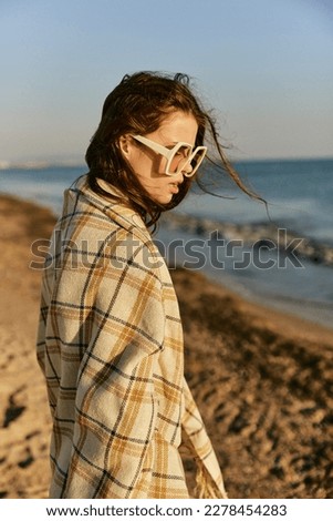 portrait of a beautiful woman with red hair blown by the wind on the sea coast, wrapped in a plaid and lowering her head down