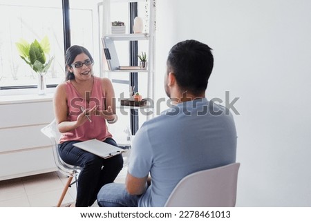 Hispanic young woman psychologist with male patient telling about mental problems while doctor is listening and making notes. Psychotherapy concept in Mexico Latin America Royalty-Free Stock Photo #2278461013