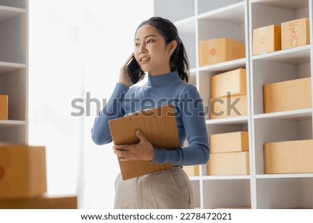 Startup, small business, SME, Asian female entrepreneur owner uses smartphones to talk to customers online and check online orders to prepare packages. Sell Ideas Online. Royalty-Free Stock Photo #2278472021
