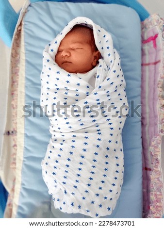 a newborn baby boy who is just 1 day old is swaddled wrapped in a muslin cloth to make him feel cozy as his mothers womb Royalty-Free Stock Photo #2278473701